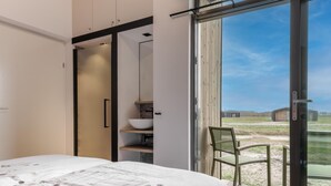 Quarto com uma cama grande, porta de correr para uma varanda e vista do campo.