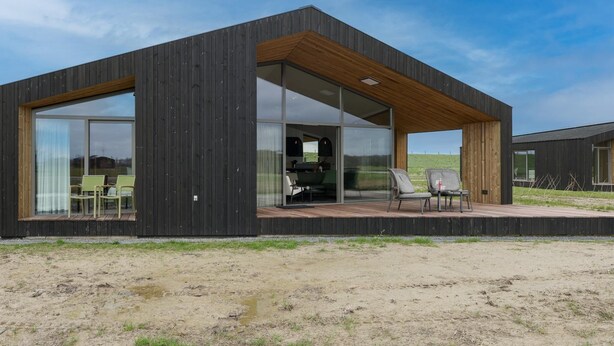 Uma casa moderna com uma grande porta de vidro, um deck de madeira e área de estar externa.