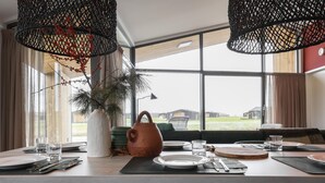 Uma área de jantar com uma mesa posta para dois, uma planta em vaso e vista para o exterior.