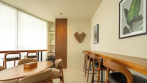 A modern dining area with a wooden table and chairs, a small kitchen area, and a wall-mounted shelf with decorative items. - Romantic 1BR Villa Canggu Pool & Sunset Balcony (Canggu)