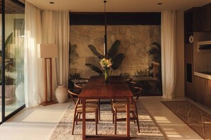 A dining area with a wooden table, chairs, a vase with flowers, and a stone wall. - Romantic 1BR Villa Canggu Pool & Sunset Balcony (Canggu)
