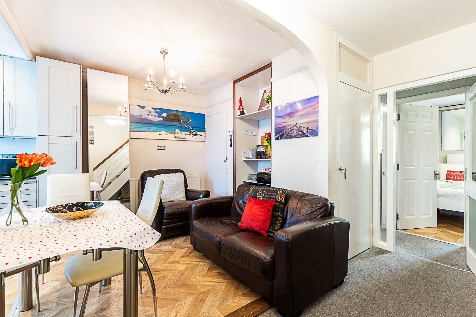 A compact living space with a dining area, a sofa, a chair, a table with a vase of flowers, and artwork on the walls.
