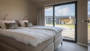 Une chambre avec un grand lit, deux lampes de chevet et une vue sur un immeuble par une porte-fenêtre coulissante.