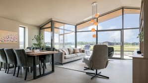 Un salon moderne avec un coin repas, de grandes fenêtres et une vue sur l’extérieur.