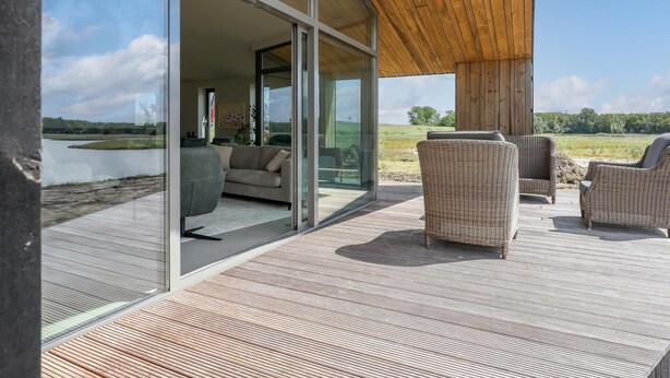 Une maison moderne dotée de grandes portes vitrées donnant sur une terrasse extérieure aménagée avec des meubles en osier.