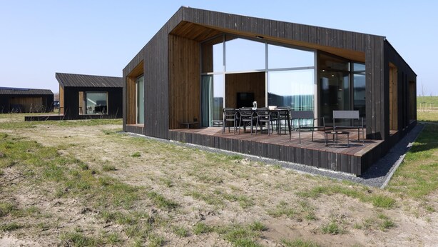 Ein modernes Gebäude mit großen Fenstern, einer Terrasse und einem Essbereich.