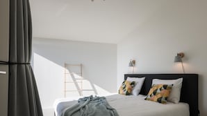 Ein Schlafzimmer mit einem Bett, Kissen, einer Decke, einer Leiter und Wandleuchten.