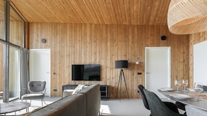 Ein modernes Interieur mit Holzwandverkleidung, einem Flachbildfernseher, einer Couch, einem Esstisch mit Stühlen und einer Stehlampe.