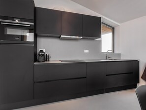 A modern kitchen with dark cabinetry, a built-in oven, and a coffee machine. - Nature house with veranda and rain shower (Wissenkerke)