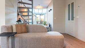 Ein modernes Wohnzimmer mit einer gebogenen Couch, einem kleinen Tisch, einer Wendeltreppe und Blick auf den Essbereich.