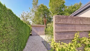 Ein Kiesweg führt zu einer Holzhütte, umgeben von einer ordentlich geschnittenen Hecke und viel Grün.