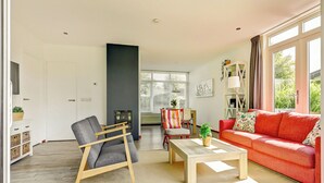 Ein modernes Wohnzimmer mit einem roten Sofa, einem grauen Sessel, einem Holztisch und einem Essbereich im Hintergrund.