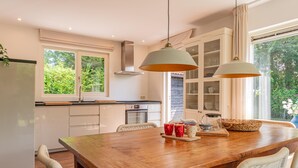 Eine moderne Küche mit Esstisch aus Holz, weißen Schränken und einem großen Fenster.