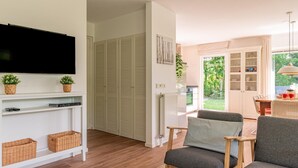 Ein Wohnzimmer mit Fernseher, Korbwannen, einer Couch und einem Essbereich mit Tisch und Stühlen.