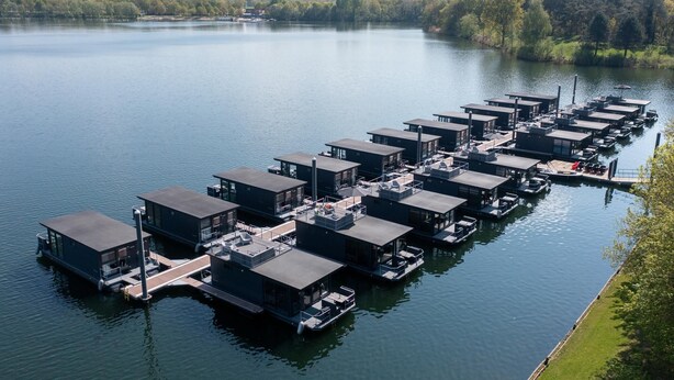 Een reeks drijvende constructies met balkons en ramen, afgemeerd aan een kalme plas.