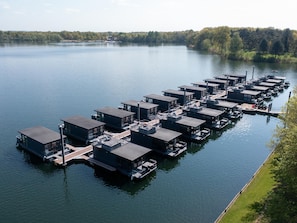 Een reeks drijvende constructies met balkons en ramen, afgemeerd aan een kalme plas.