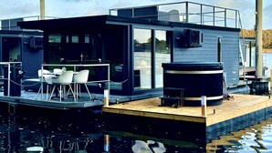 Een moderne drijvende constructie met terras, buitenmeubels en een hottub.