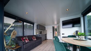 Een modern interieur met een bank, eettafel, stoelen, een keuken en een aan de muur bevestigde televisie.
