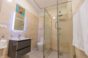 Een moderne badkamer met een douchecabine van glas, een wastafel met spiegel en een toilet.
