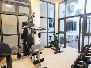 Een sportschool met trainingsapparatuur, grote ramen en uitzicht op buiten.