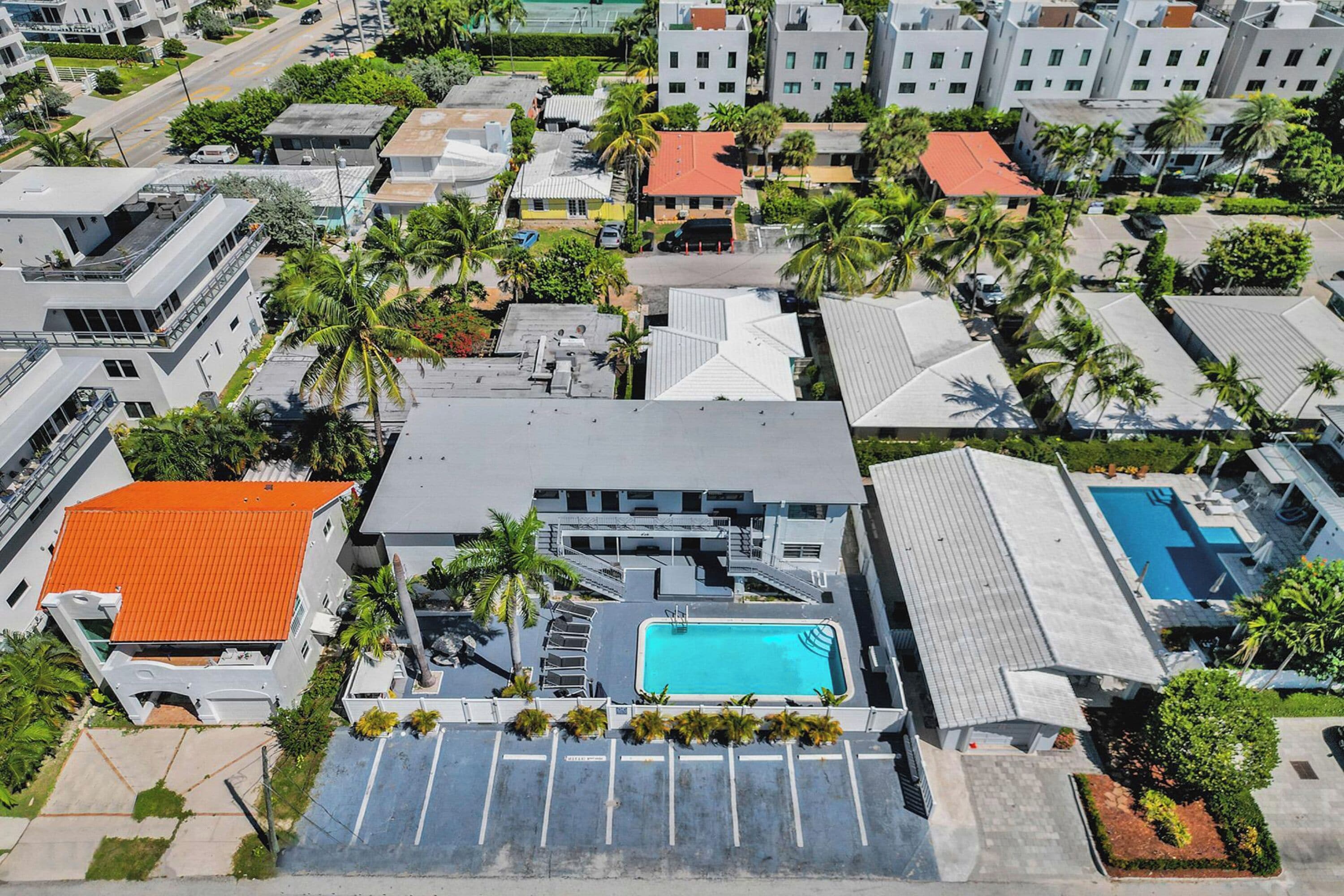 Oversigtsbillede af et boligområde med moderne bygninger, en swimmingpool og palmer.