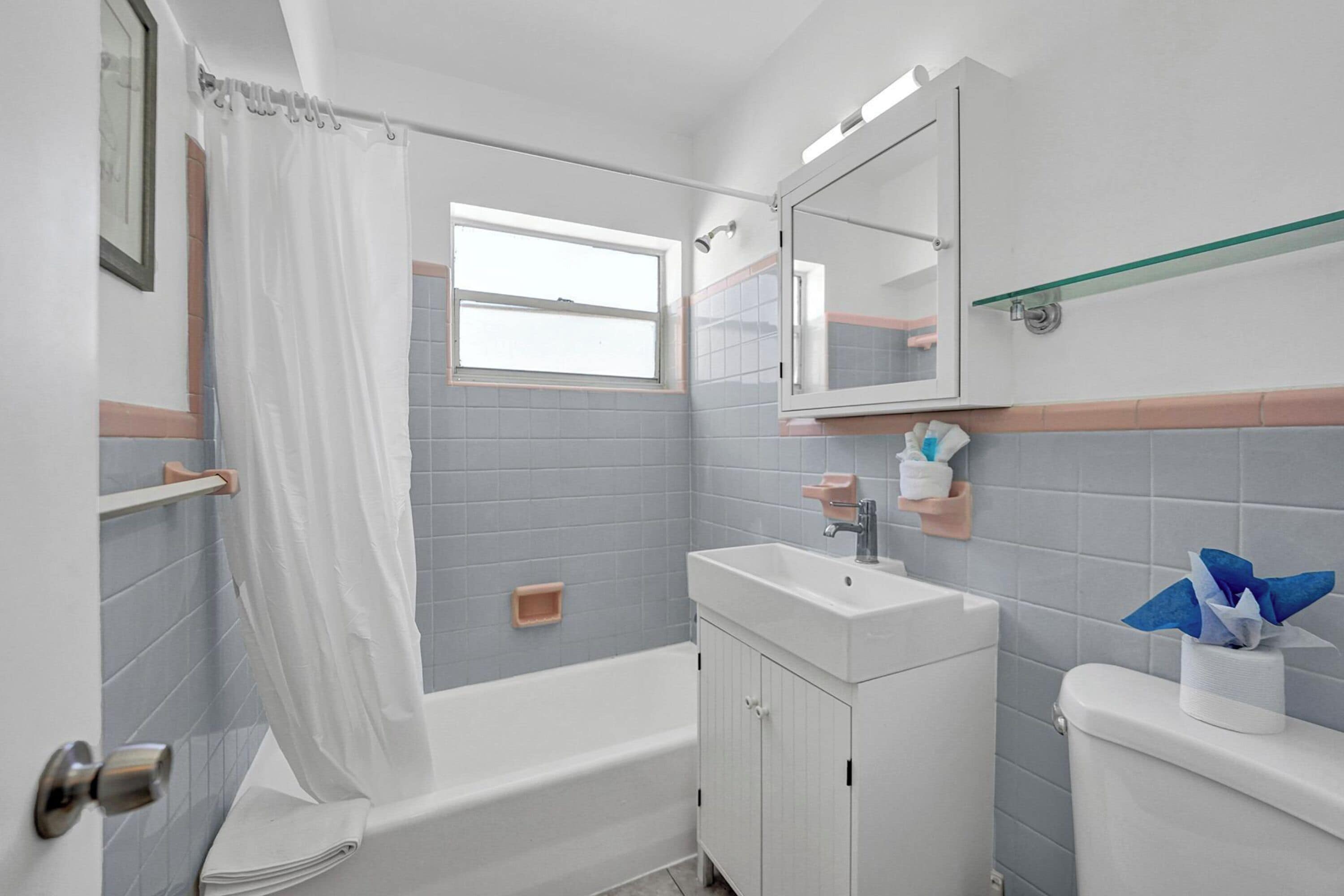 A bathroom with a bathtub, a sink, a mirror, and a window.