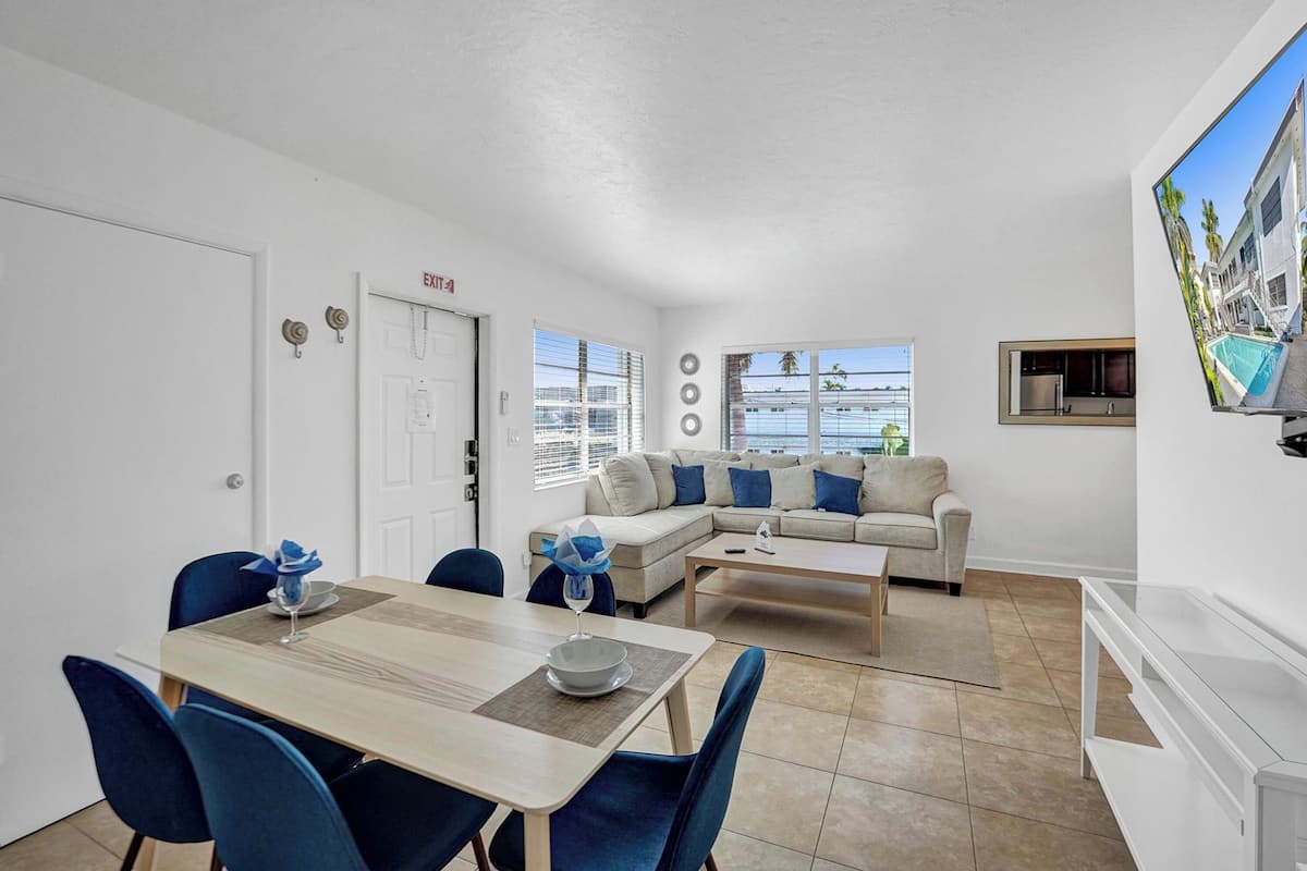 A modern living room with a dining area, a sofa set, and a TV on the wall.