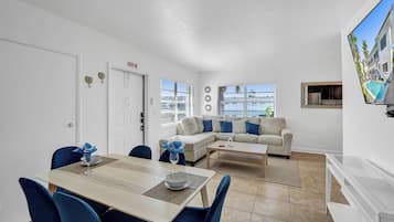 Una sala de estar moderna con comedor, un conjunto de sofás y un televisor en la pared.