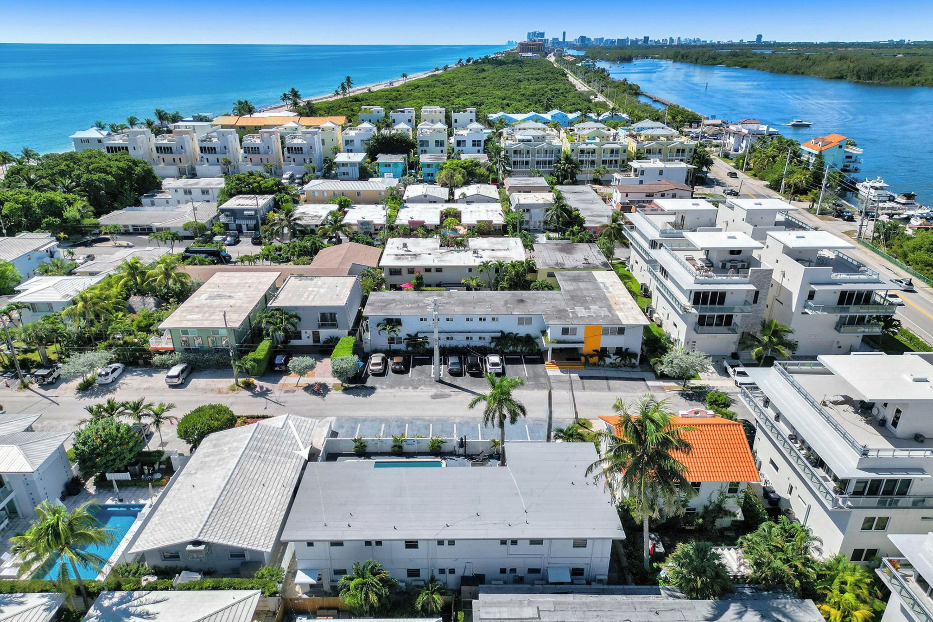 An aerial view of a coastal residential area with buildings, a swimming pool, and a view of the ocean.