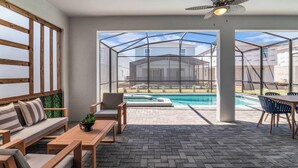 A sunlit patio with a pool, wooden furniture, and a view of a house through large windows. - Themed 7BR Villa | Lion King · Frozen · Minions | Mario Game Room | Pool & Spa (Clermont)