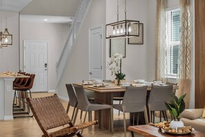 A modern dining area with a wooden table, grey chairs, and a hanging light fixture. - Themed 7BR Villa | Lion King · Frozen · Minions | Mario Game Room | Pool & Spa (Clermont)