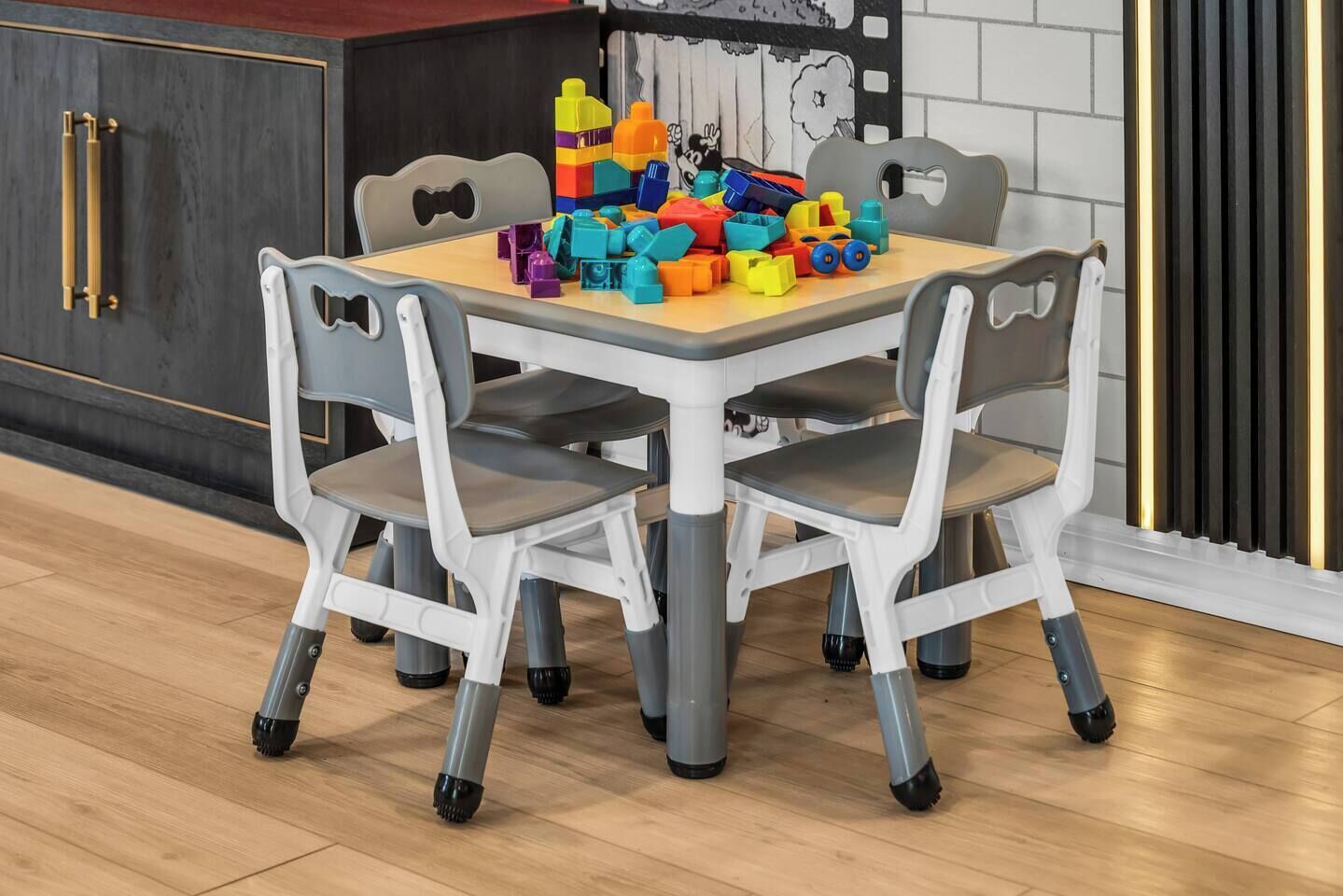 Un coin repas avec une table et quatre chaises, un ensemble de jouets colorés posé sur la table, et une cuisine avec des meubles sombres et un plan de travail blanc.