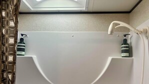 A bathroom with a shower enclosure, a towel rack, and two bottles of shampoo. - Charming Charlevoix Camper Getaway Near Lake Michigan (Charlevoix)