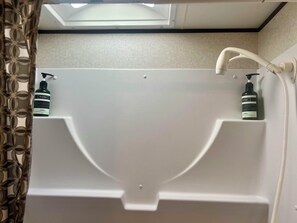 A bathroom with a shower enclosure, a towel rack, and two bottles of shampoo. - Charming Charlevoix Camper Getaway Near Lake Michigan (Charlevoix)