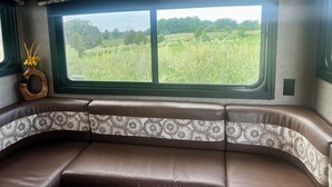A vehicle interior with a large window, a cushioned bench, and a decorative vase. - Charming Charlevoix Camper Getaway Near Lake Michigan (Charlevoix)