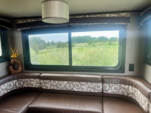 A vehicle interior with a large window, a cushioned bench, and a decorative vase. - Charming Charlevoix Camper Getaway Near Lake Michigan (Charlevoix)