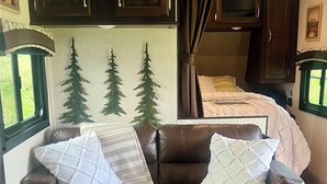 A cozy living area with a brown leather sofa, a matching ottoman, and a window with curtains. - Charming Charlevoix Camper Getaway Near Lake Michigan (Charlevoix)