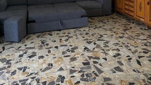 Een woonkamer met een hoekbank, een decoratief schilderij, een houten kast en een betegelde vloer.