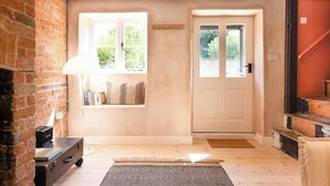 Una habitación con pared de ladrillo, una puerta blanca, ventana con vistas, una lámpara y una pequeña mesa.