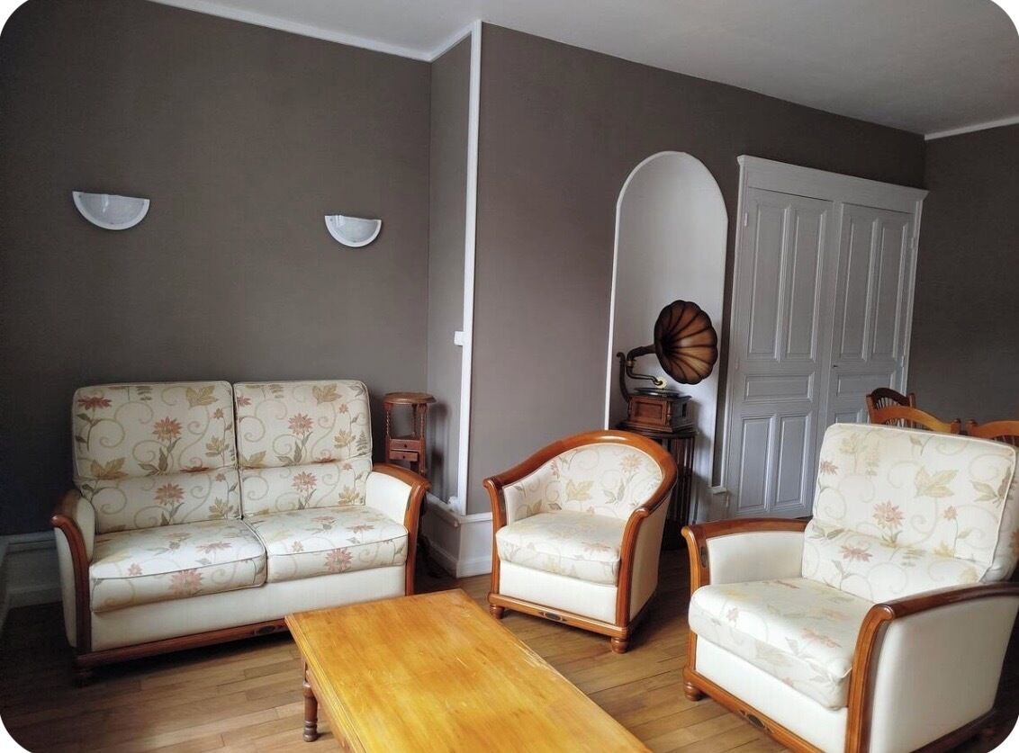 A living room with a sofa, two armchairs, a wooden coffee table, and a white door with a decorative mirror.