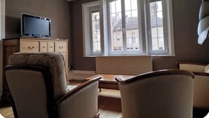 Ein Wohnzimmer mit Fernseher, einer Couch, einem Sessel und einem Fenster mit Blick auf Gebäude.
