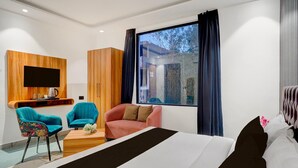 A modern hotel room with a bed, two chairs, a small table with a kettle, a TV mounted on a wooden panel, and a large window with curtains. - Super Deluxe Roomtroy Resorts and Wellness (Dera Bassi)