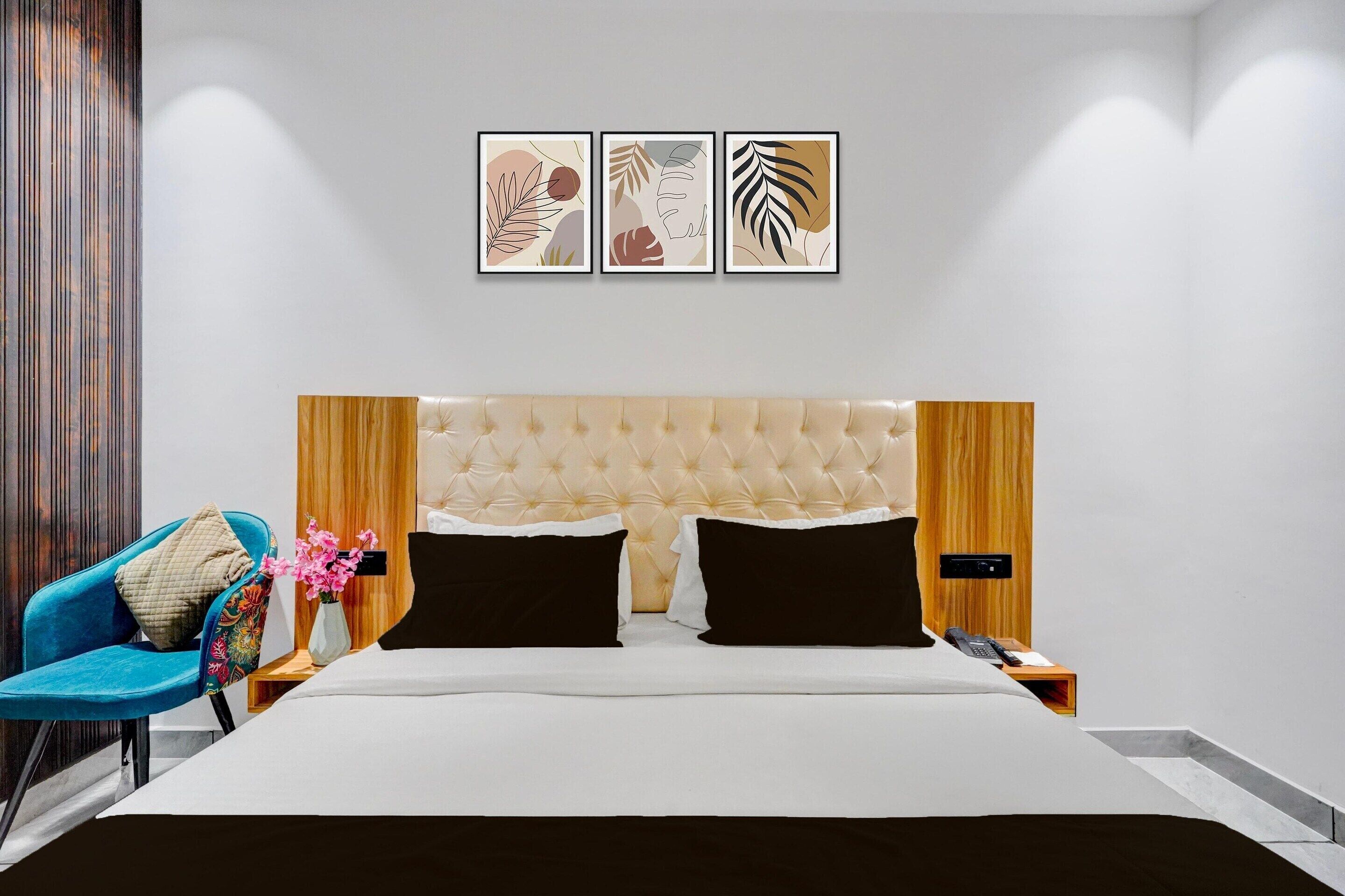 Une chambre d’hôtel moderne avec une tête de lit capitonnée, une chaise bleue, une table de chevet ornée d’un vase de fleurs et trois œuvres d’art encadrées accrochées au mur.
