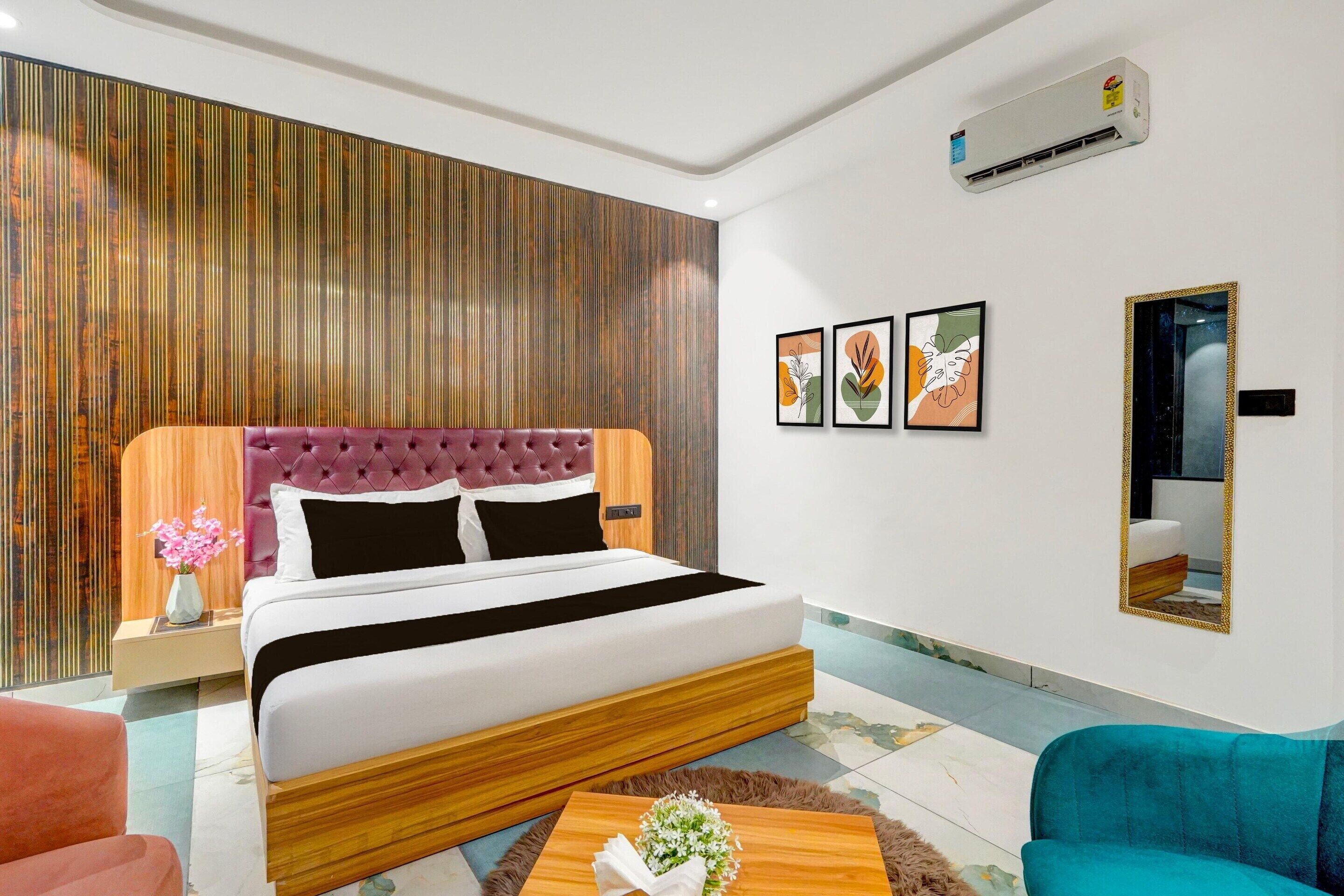 Een moderne hotelkamer met een groot bed, een houten hoofdbord, een bijzettafeltje met een vaas, een bank en een wandairconditioning.