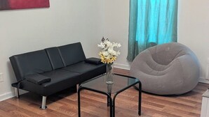 A modern living room with a black sofa, a round bean bag, and a glass coffee table with a vase of flowers.