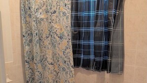 A bathroom with a patterned shower curtain, a bathtub, and a window with a plaid curtain.