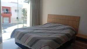 Et soveværelse med en stor seng, et træhovedgærde, en glasdør til en balkon og udsigt til bygninger.
