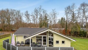 Ett enplanshus med ett sluttande tak, en täckt uteplats med utemöbler och en inhägnad trädgård.