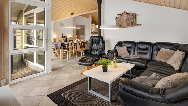 Ett modernt vardagsrum med en soffa i läder, en matplats med stolar i trä och ett kök i bakgrunden.