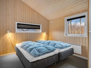 A room with wooden walls, a bed with blue bedding, a window with a view of trees, and a wall-mounted air conditioning unit. - "Erikka" - 40km from the sea by Interhome (Ansager)